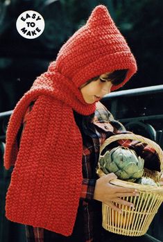 a woman wearing a red knitted hat and scarf holding a basket full of vegetables