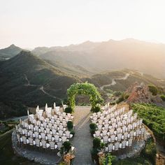 an outdoor ceremony setup with white chairs and greenery in the foreground, surrounded by mountains