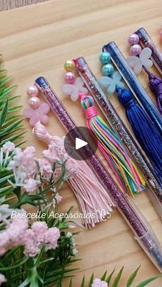 several pencils with tassels and beads are on a wooden table next to flowers