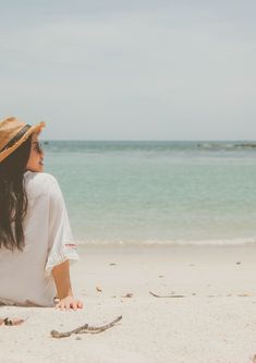 a woman sitting on the beach looking out at the ocean