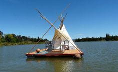 a teepee sitting on top of a body of water next to a boat with poles sticking out of it