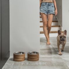 a woman walking down the hall with her dog and two bowls on the floor in front of her