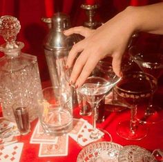 a woman's hand reaching for some wine glasses on a table with other items