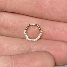 a person's hand holding a gold nose ring with small white stones on it