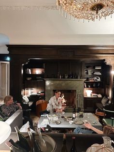 people sitting around a living room table in front of a fire place with wine bottles on it