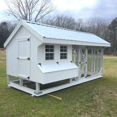 a small white chicken coop in the middle of a field