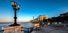 a street light on the side of a road next to some water with buildings in the background