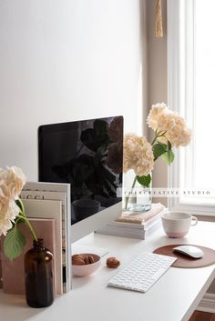 a white desk with flowers, books and a computer monitor on it's side