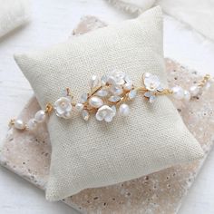 a white pillow sitting on top of a table next to a gold and pearl bracelet