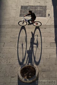 the shadow of a person riding a bike on a sidewalk next to a drain hole