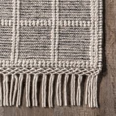 a white and gray rug with fringes on top of a wooden floor next to a wall