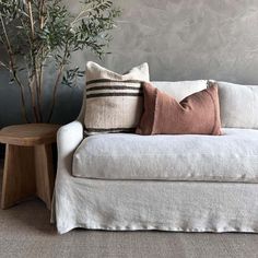 a white couch with pillows on it next to a small table and potted plant