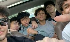 a group of young men sitting in the back seat of a car with their hands up