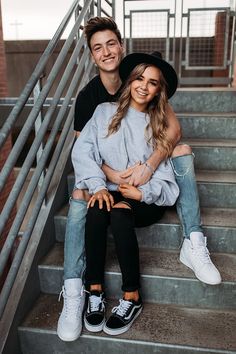 a man and woman sitting on the steps smiling at the camera with their arms around each other