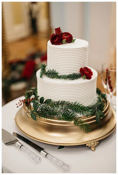 a three tiered white cake with red flowers on top sits on a gold platter