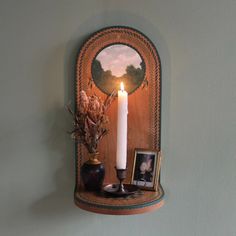 a candle is lit on top of a shelf with pictures and vases next to it