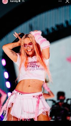 a woman with pink hair wearing a white shirt and skirt while standing in front of a crowd