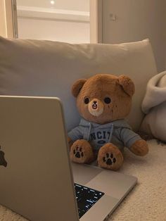 a brown teddy bear sitting on top of a couch next to an apple laptop computer