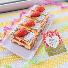 a white plate topped with cake covered in powdered sugar and strawberries next to a card