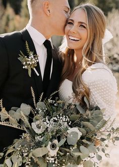 a bride and groom kissing each other with greenery in the foreground on their wedding day