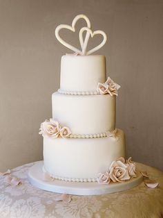 a white wedding cake with two hearts on top