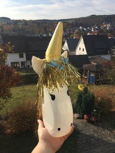 a hand holding up a plastic unicorn mask in front of a house with trees and houses in the background