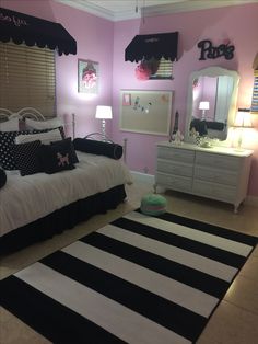 a bedroom with pink walls, black and white bedding, and striped rugs