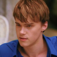 a close up of a person wearing a blue shirt and looking at the camera with a serious look on his face