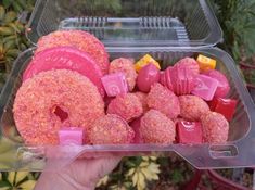 a plastic container filled with donuts covered in pink sprinkles and candy