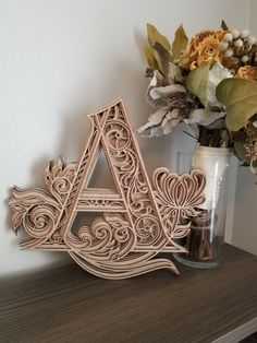 a wooden letter sitting on top of a table next to a vase with flowers