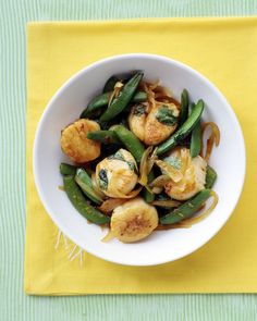 a bowl filled with green beans and scallops on top of a yellow napkin