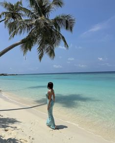 a woman in a blue dress standing on a beach next to the ocean and palm trees