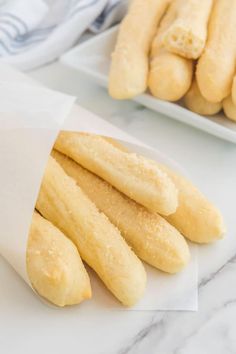 bread sticks sitting on top of a white plate next to a bowl of doughnuts