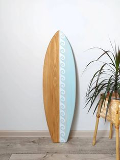 a wooden surfboard next to a potted plant on the floor in front of a white wall