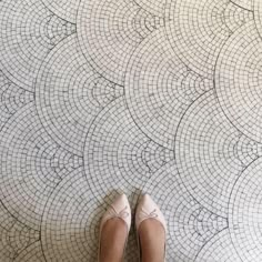 a woman standing on the floor in front of a wall with an intricate tile design