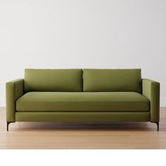 a green couch sitting on top of a hard wood floor next to a white wall