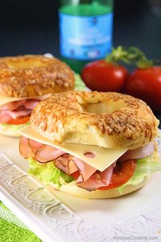 two sandwiches with meat, cheese and tomatoes on a white plate next to a knife