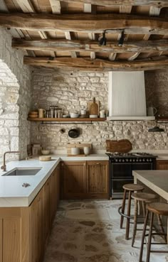 a kitchen with stone walls and flooring next to a stove top oven under a wooden ceiling