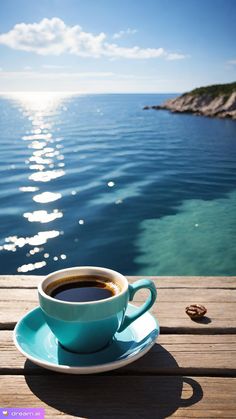 a cup of coffee sitting on top of a wooden table next to the ocean,