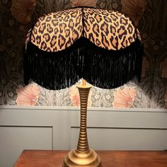 a lamp with a leopard print shade on it and a black fringe around the base