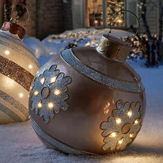 two christmas ornaments sitting in the snow near a house with lights on it's sides