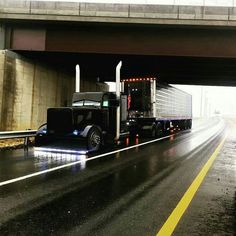 a semi truck driving under an overpass in the rain