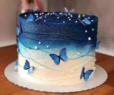 there is a blue and white cake with butterflies on the frosting, sitting on top of a wooden table