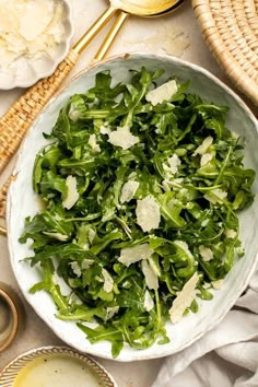 a white bowl filled with greens and cheese on top of a table next to bread