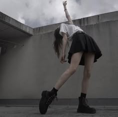 a woman in black and white is reaching up into the air with her hand while standing on concrete