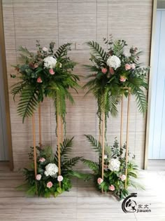 two tall planters with flowers and greenery are on display in front of a wall