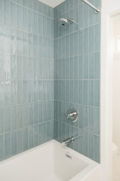 a bath tub sitting under a window next to a tiled wall and white tile floor