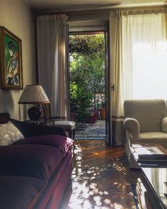 a living room filled with furniture next to a window covered in sun shining through the curtains