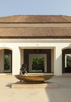 a woman sitting on top of a golden bowl in front of a white building with arches