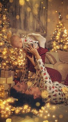 a woman laying on the floor with a baby in her lap next to a christmas tree